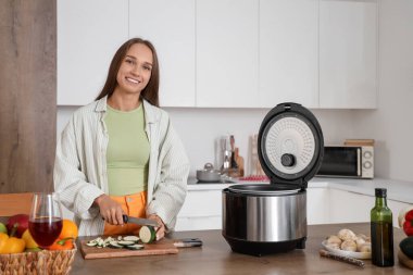 Mutfaktaki masada çoklu tencereyle kabak kesen genç bir kadın.