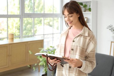 Dua boncuklarıyla evde İncil okuyan güzel genç bir kadın.