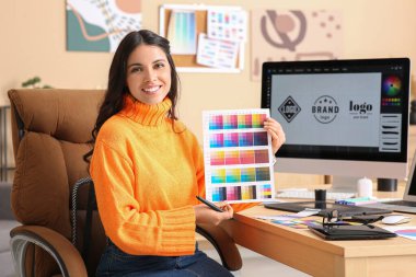 Genç bayan grafik tasarımcısı masadaki renk örnekleriyle çalışıyor.