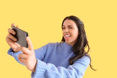 Cep telefonlu güzel bir kadın sarı arka planda selfie çekiyor.