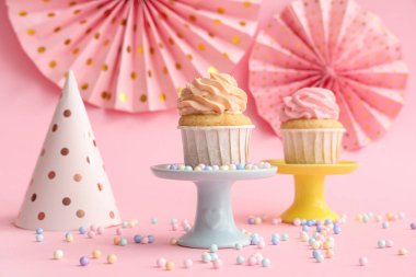 Tatlı doğum günü kekleri, serpiştirmeler ve pembe arka planda parti şapkası