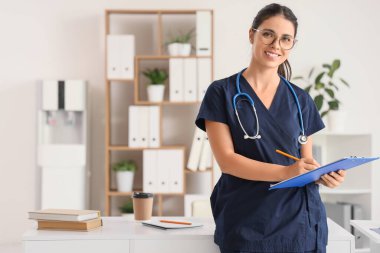 Klinikte klasörü ve steteskopu olan genç bir tıp öğrencisi.