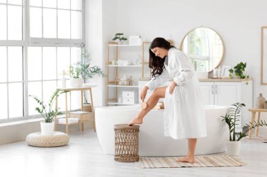 Güzel, genç, mutlu bir kadın banyoda fırçayla bacaklarına masaj yapıyor.