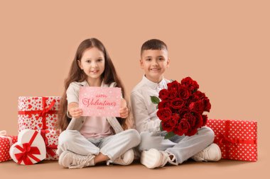 Elinde gül buketi, tebrik kartı ve bej arka planda duran hediye kutuları olan şirin çocuklar. Sevgililer Günü kutlaması