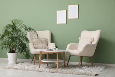 Koltuklar ve sehpa yeşil duvarın yanında.