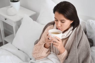 Hasta genç kadın yatakta sıcak çay içiyor.