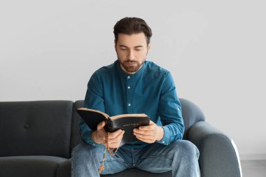Evdeki kanepede oturan adam İncil okuyor.