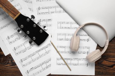 Dizüstü bilgisayarlı müzik kağıtları, kulaklıklar ve tahta arka planda gitar.