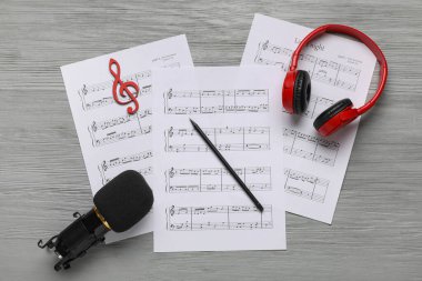 Kulaklıklı müzik kağıtları ve gri ahşap arka planda mikrofon.