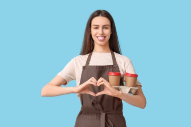 Kahveli genç bayan barista mavi arka planda kalp hareketi yapıyor.