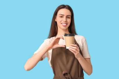 Kahveli genç bayan barista mavi arka planda kalp hareketi yapıyor.