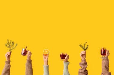 Turuncu, köknar ağacı dallı kadın eller ve sarı arka planda lezzetli sıcak şarap kadehleri.