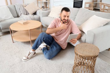 Evdeki halıda tablet bilgisayar kullanan genç adam.
