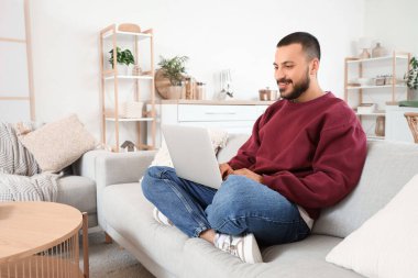 Evde kanepede dizüstü bilgisayar kullanan genç adam