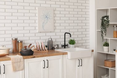 Mutfak tezgahında lavabo ve çatal bıçak beyaz tuğla duvarın yanında.