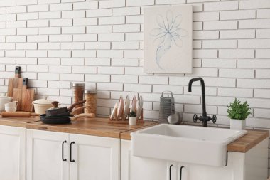 Lavabo, ev bitkileri ve çatal bıçaklar mutfaktaki beyaz tuğla duvarın yanında.
