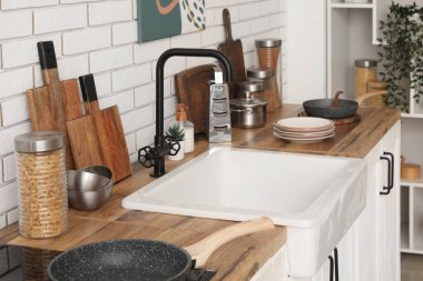 Mutfaktaki beyaz tuğla duvarın yanında farklı mutfak aletleri ve lavabo.