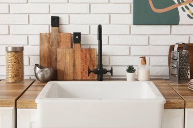 Mutfaktaki beyaz tuğla duvarın yanında lavabo ve çatal bıçaklarla dolu bir masa.