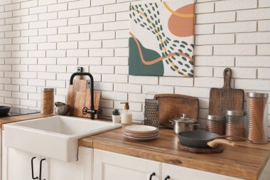 Mutfaktaki beyaz tuğla duvarın yanında lavabo ve çatal bıçaklarla dolu bir masa.