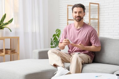 Şeker hastası genç adam evdeki kanepede tükenmez kalem kullanıyor.