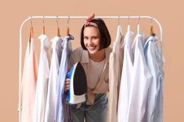 Bej arka planda demir ve elbise askısı olan gülümseyen genç bir kadın.