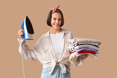 Bej arka planda demir ve giysi yığını ile gülümseyen genç kadın.