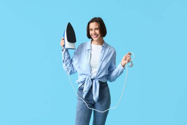 Mavi arka planda demiri olan gülümseyen genç kadın.