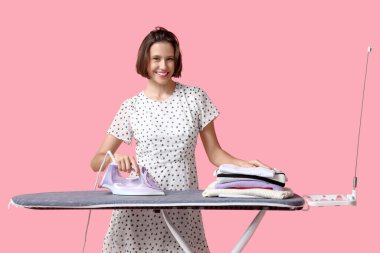 Gülümseyen genç kadın pembe arka planda ütü yapıyor.