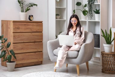 Çizgili pijamalarıyla evde dizüstü bilgisayarla çalışan serbest çalışan bir kadın.