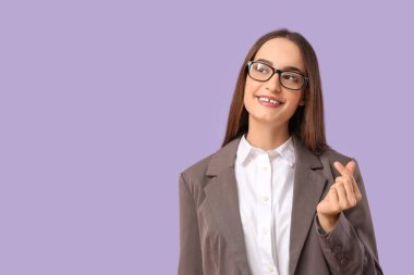 Güzel genç bir kadın parmaklarıyla leylak arka planda kalp yapıyor.