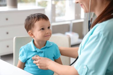 Steteskoplu kadın çocuk doktoru. Klinikte küçük şirin bir çocuğu dinliyor.