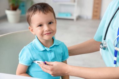 Klinikte küçük çocuğun ateşini ölçen kadın çocuk doktoru.