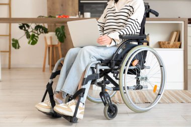 Tekerlekli sandalyede dizüstü bilgisayar kullanan genç bir kadın.