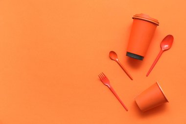 Turuncu arka planda kağıt bardaklar ve plastik çatal bıçak takımı.