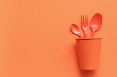 Turuncu arka planda kağıt bardak ve plastik çatal bıçak takımı.