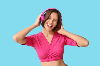 Şık tişörtlü ve kulaklıklı genç bir kadın pembe arka planda müzik dinliyor.