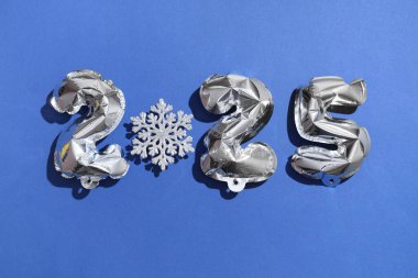 Şekil 2025 şeklindeki hava balonları. Mavi arka planda güzel bir kar tanesi var.