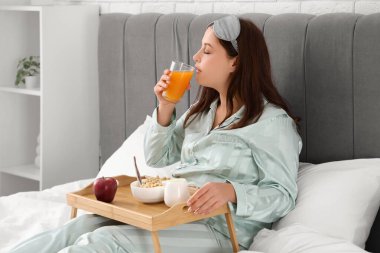 Genç ve güzel bir kadın sabah kahvaltısını yatakta yiyor.