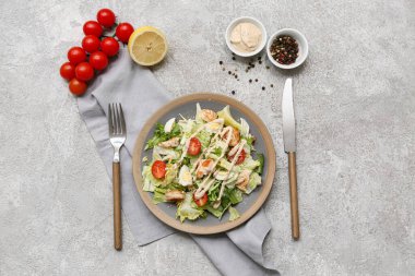 Lezzetli tavuklu Sezar salatası, limon, bir kase sos ve gri arka planda biberli mısır.