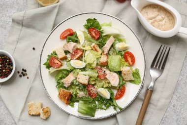 Lezzetli tavuklu Sezar salatası, biberli mısır ve gri arka planda sos teknesi.