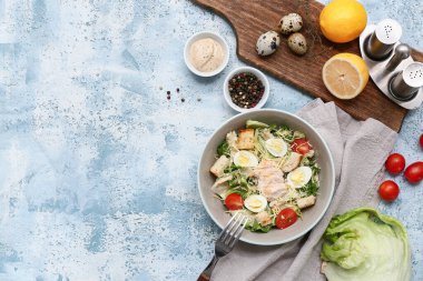 Lezzetli tavuklu Sezar salatası ve mavi arka planda malzemeler.