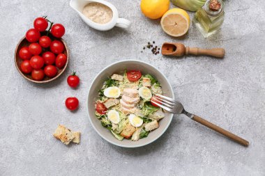 Lezzetli tavuklu Sezar salatası ve gri arka planda malzemeler.
