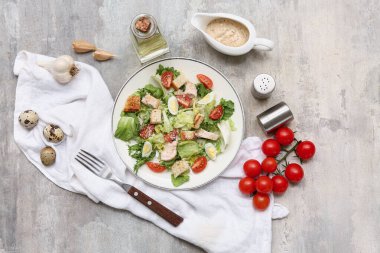 Lezzetli tavuklu Sezar salatası ve gri arka planda malzemeler.