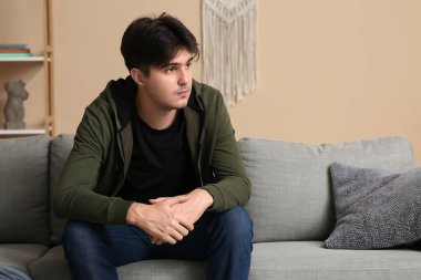 Depresyondaki genç adam evdeki kanepede oturuyor.
