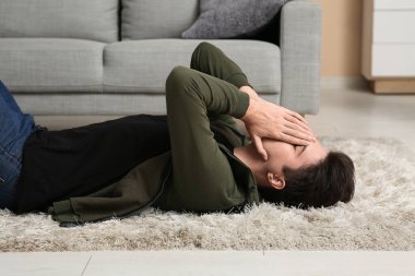Depresyondaki genç adam evde halıda yatıyor.