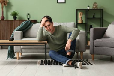 Depresyondaki genç adam evde yerde oturuyor.