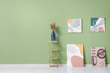 Sanat galerisindeki yeşil duvarın yanındaki rafta otlu vazolar ve güzel tablolar.