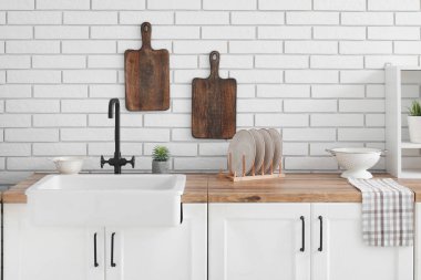 Mutfak tezgahındaki aletler beyaz tuğla duvarın yanında.