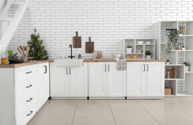 Mutfak tezgahlarındaki aletler beyaz tuğla duvarın yanında.