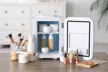 Beyaz duvarın yanındaki masada kremalı ve temeli olan küçük bir kozmetik buzdolabı. Yakın çekim.